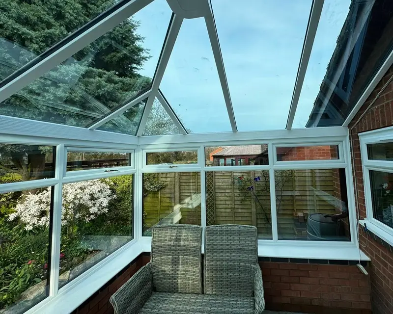 Glass roofed conservatory with a rattan sofa before replacement