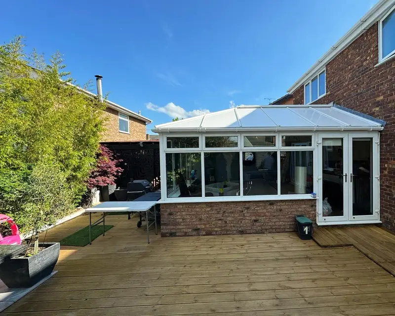 Conservatory with a white panel roof beside garden decking